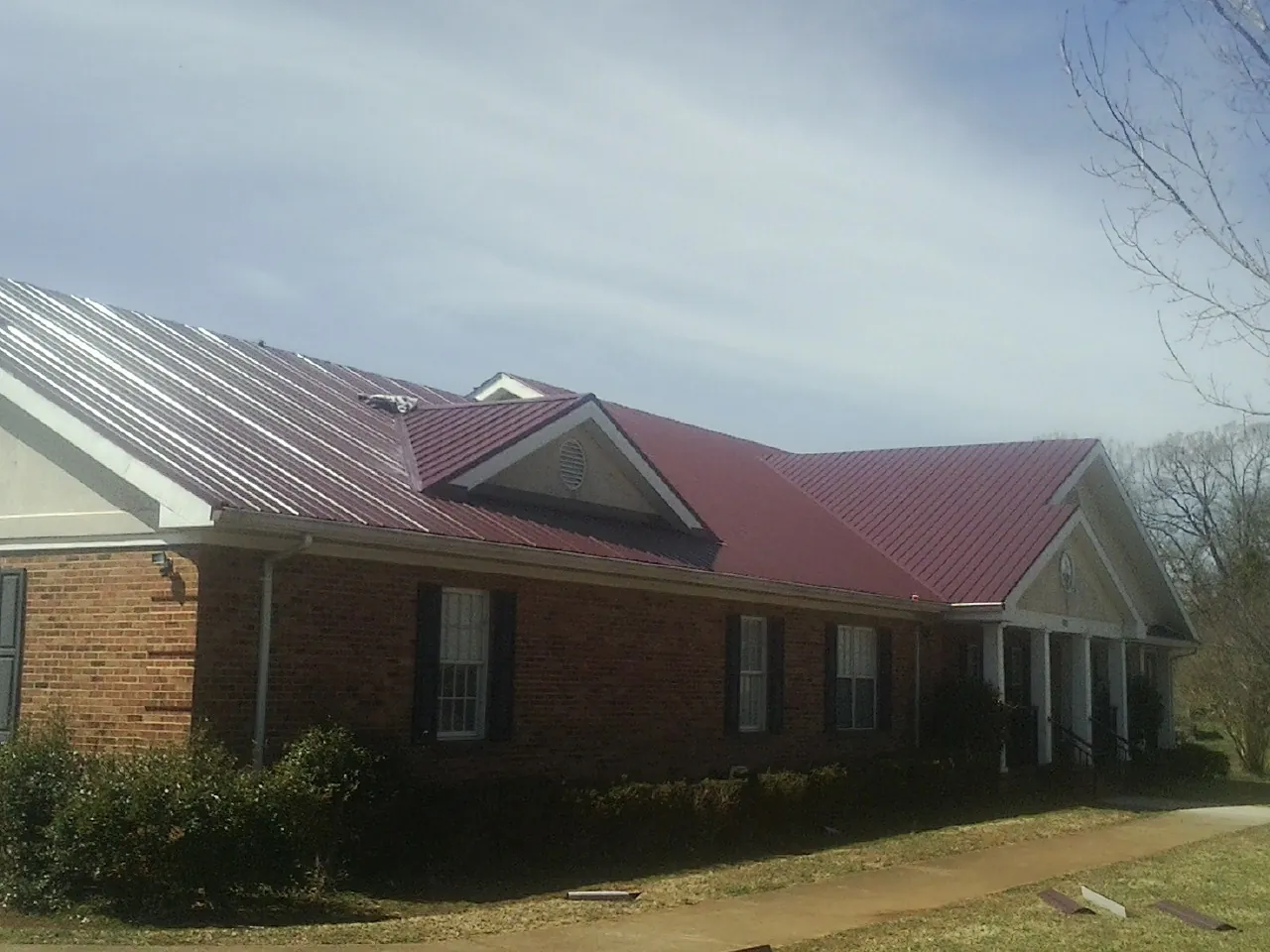 Red metal roof with gabled entries on a long brick building, from a Hail Damage Roof Repair job in Fort Ann