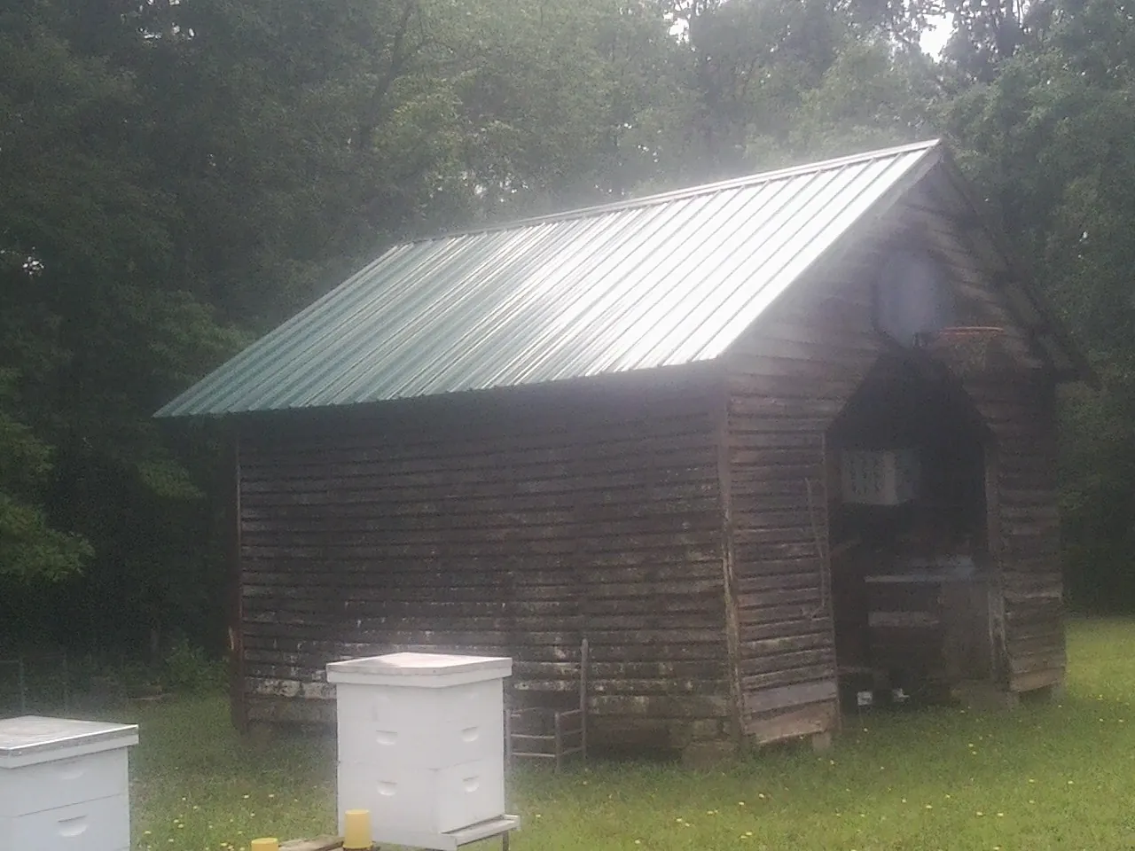 Green metal roof on a weathered barn beside stacked beehives in Fort Ann