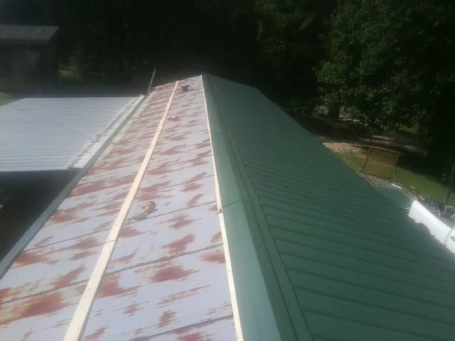 Old rusted panels beside newly installed green metal roofing — Wind Damage Roof Repair by Roofing Brothers in Fort Ann