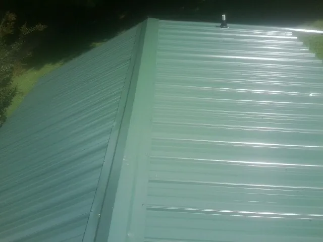 New green metal panels meeting at the ridge of a roof — Flat Roof Repair work by our crew in Fort Ann