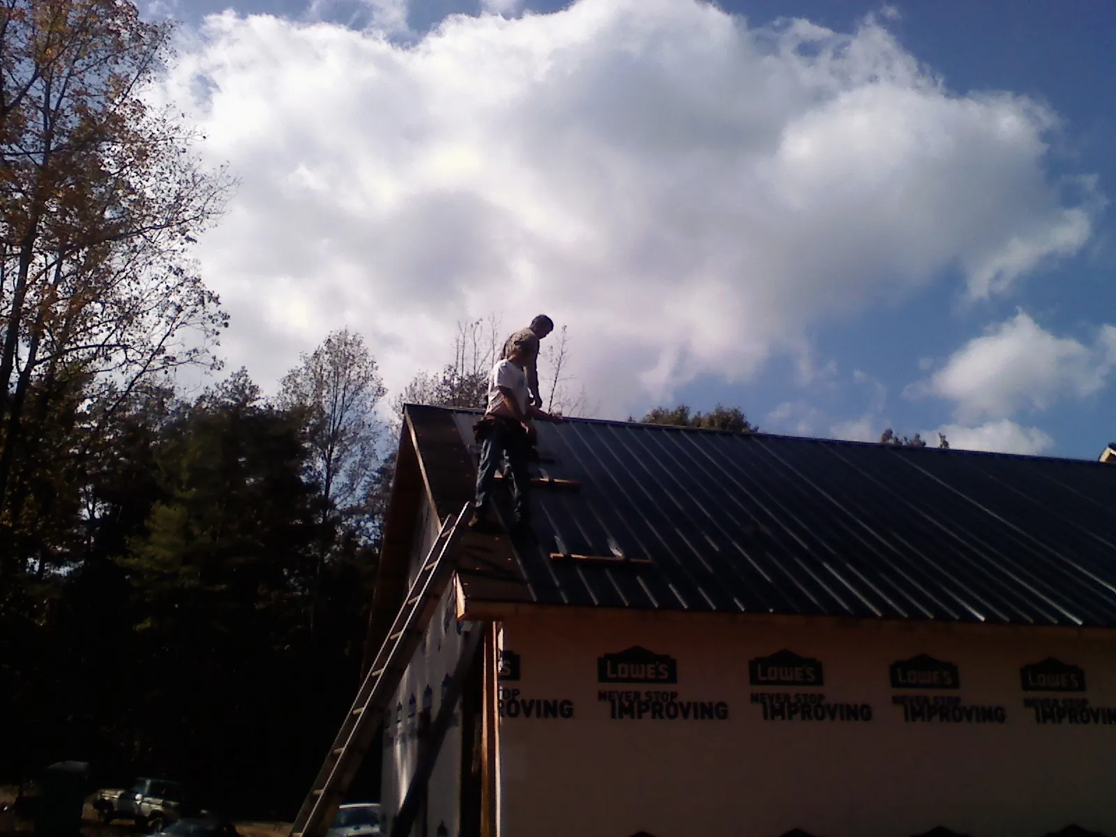Roofer fastening dark metal panels high against a cloudy sky, from a Roof Inspection job in Fort Ann