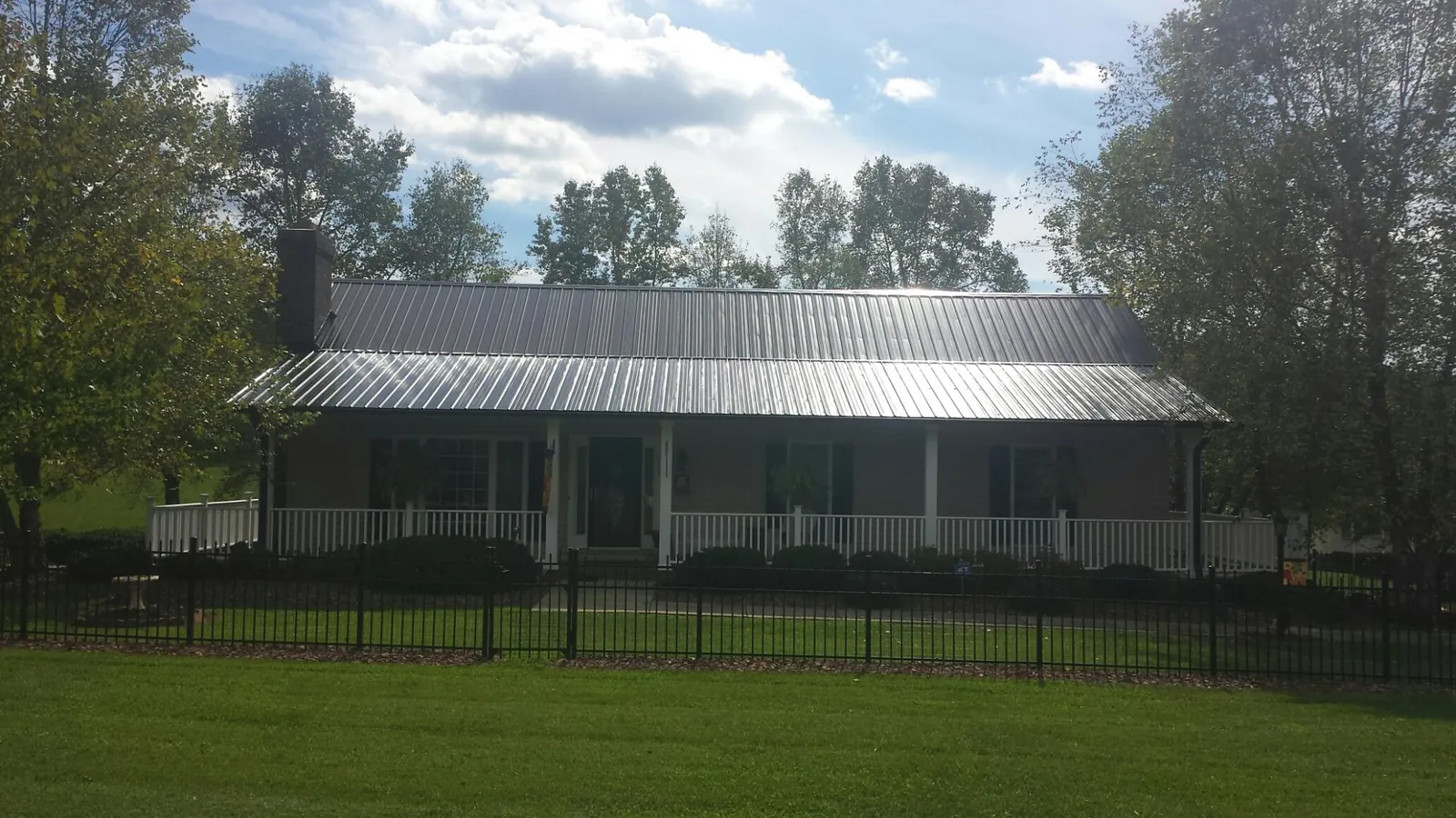 Gray metal roof on a brick ranch with a full width front porch — Gutter Guard Installation work by our crew in Fort Ann