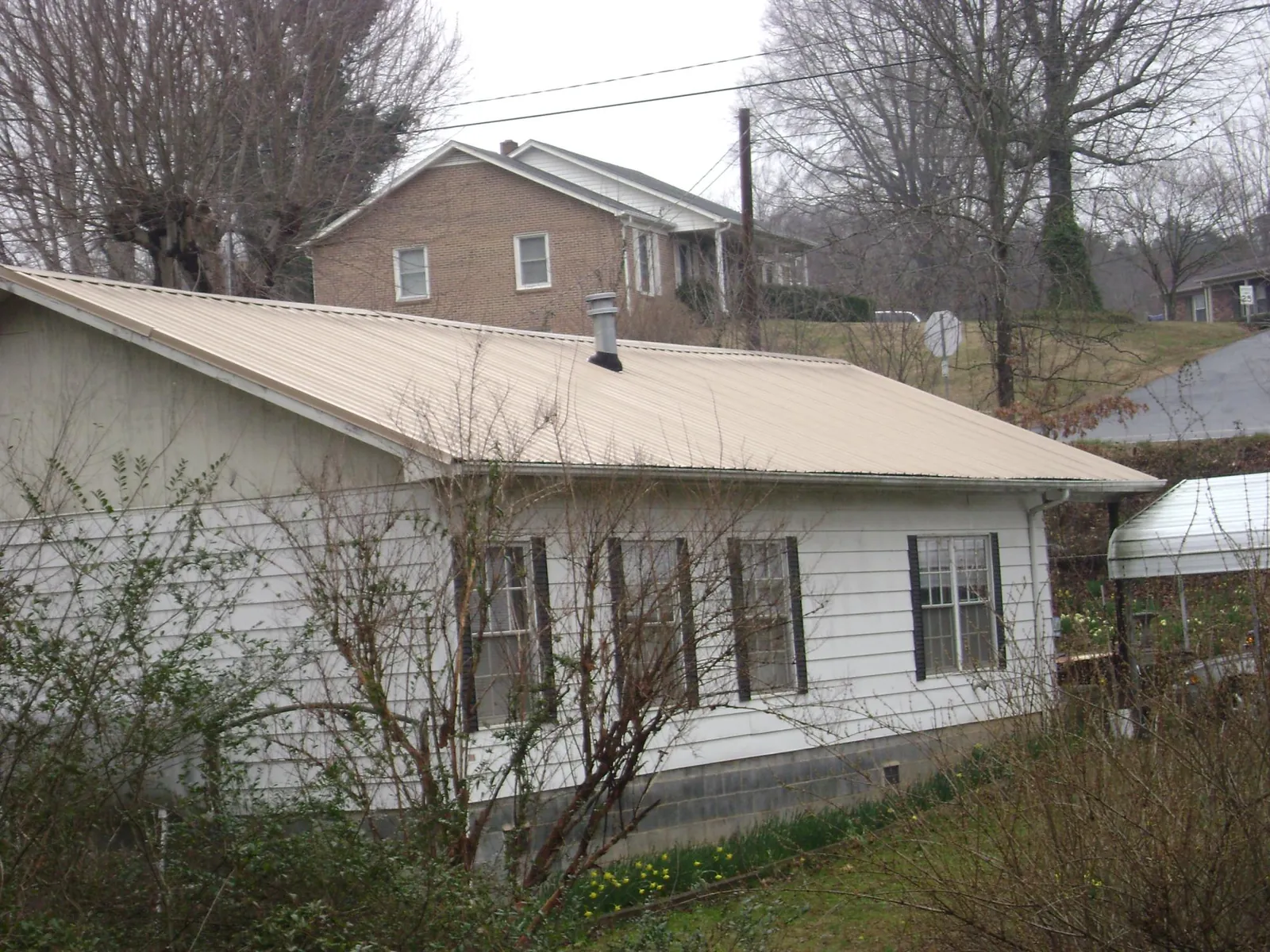 Tan metal roof on a white sided house set into a hillside — Commercial Roofing by Roofing Brothers in Fort Ann