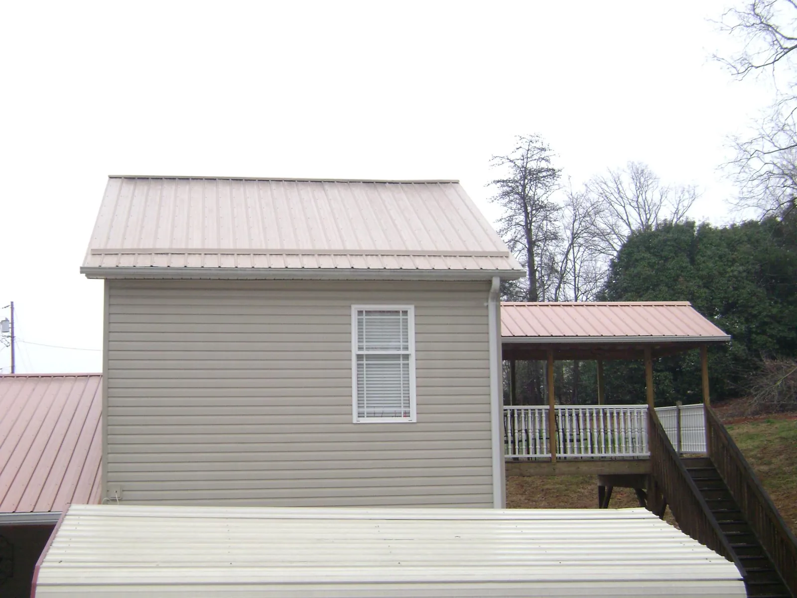 Tan metal roofs on a two story addition and attached porch, from a Roof Replacement job in Fort Ann